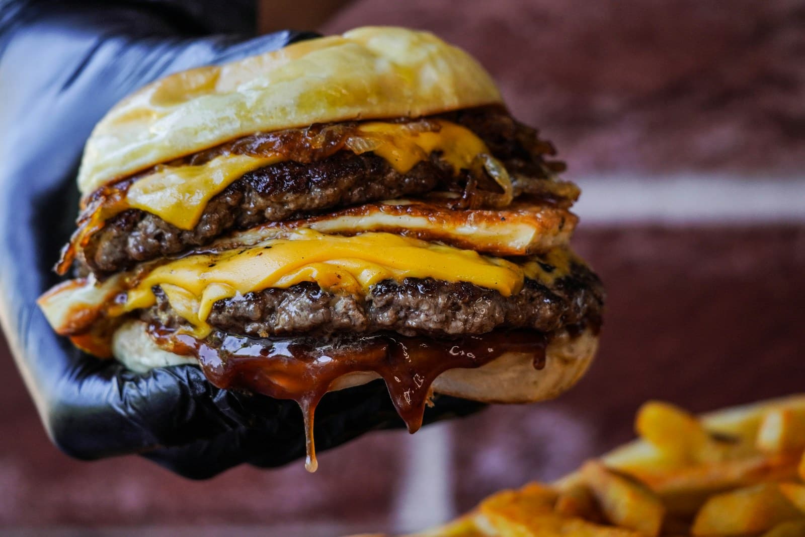 Hand holding a cheeseburger over a pile of fries