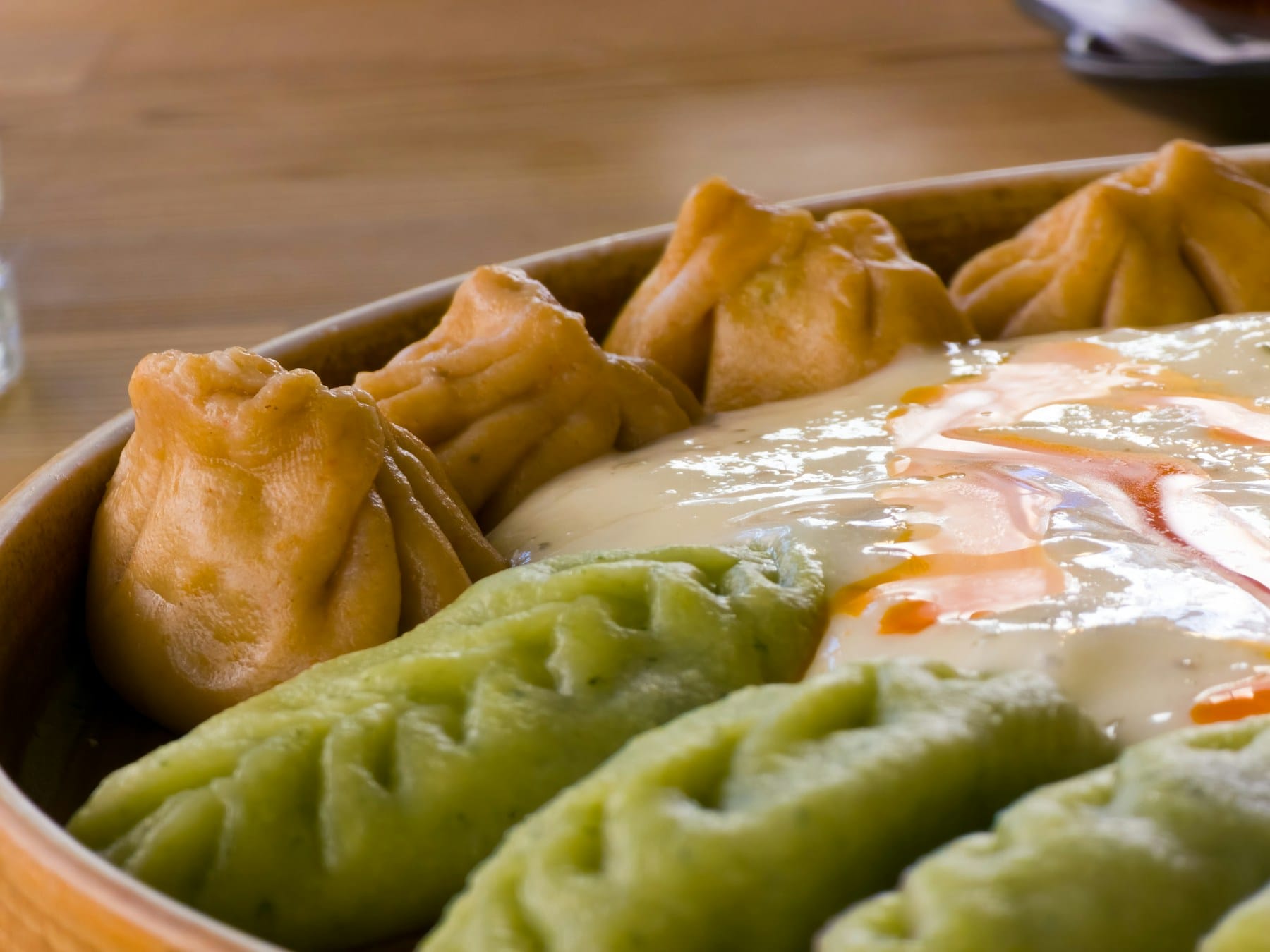 Steamed momos plated around a creamy sauce with a drizzle of chilli oil